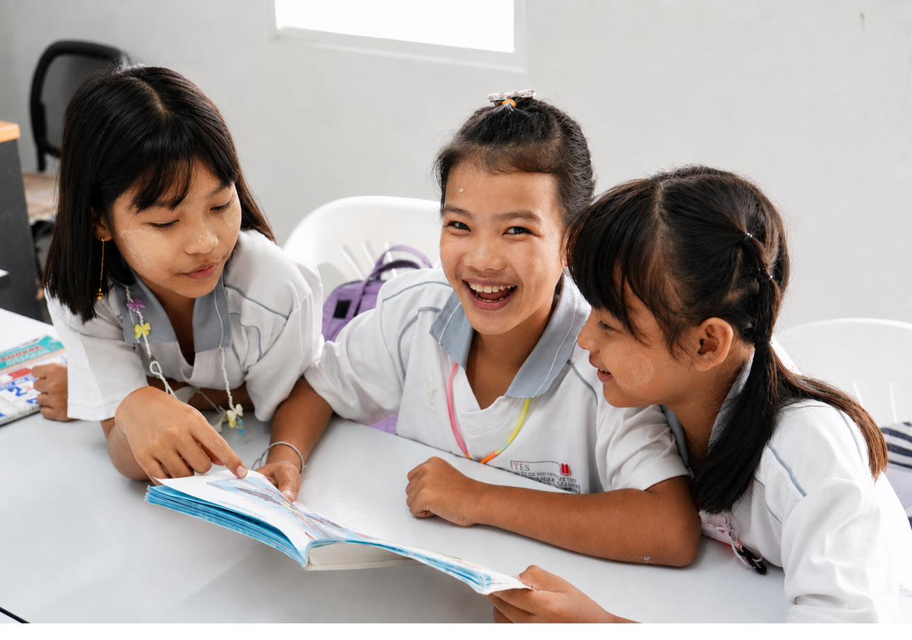 Three girls smiling and reading together over a book