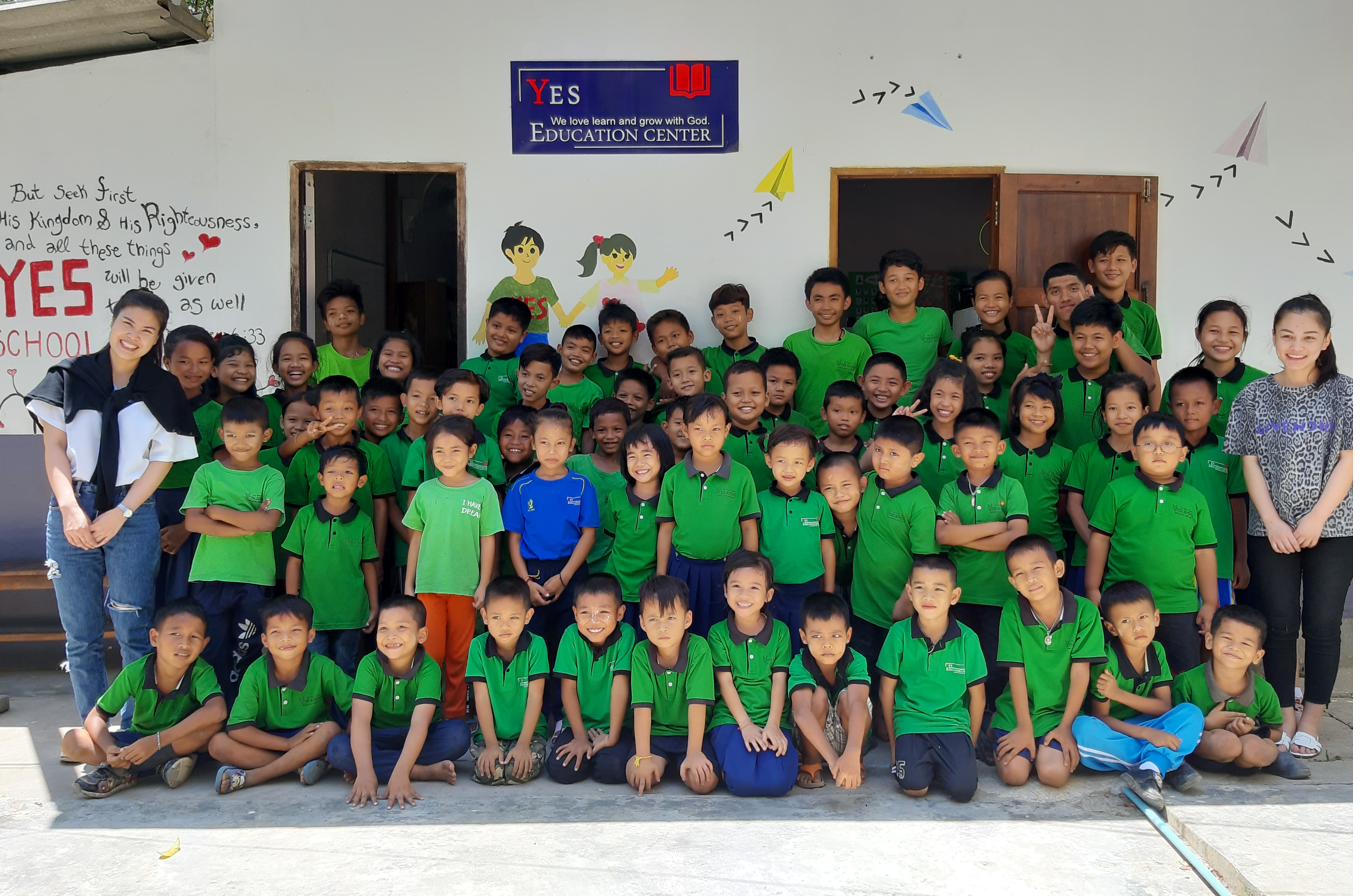 The YES Education Center sign with children and teachers gathered together, from the organization's early days